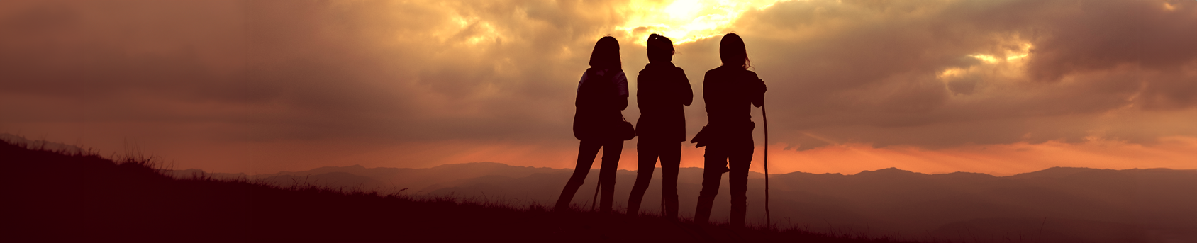 Silhouettes of three women standing on a mountain at sunrise
